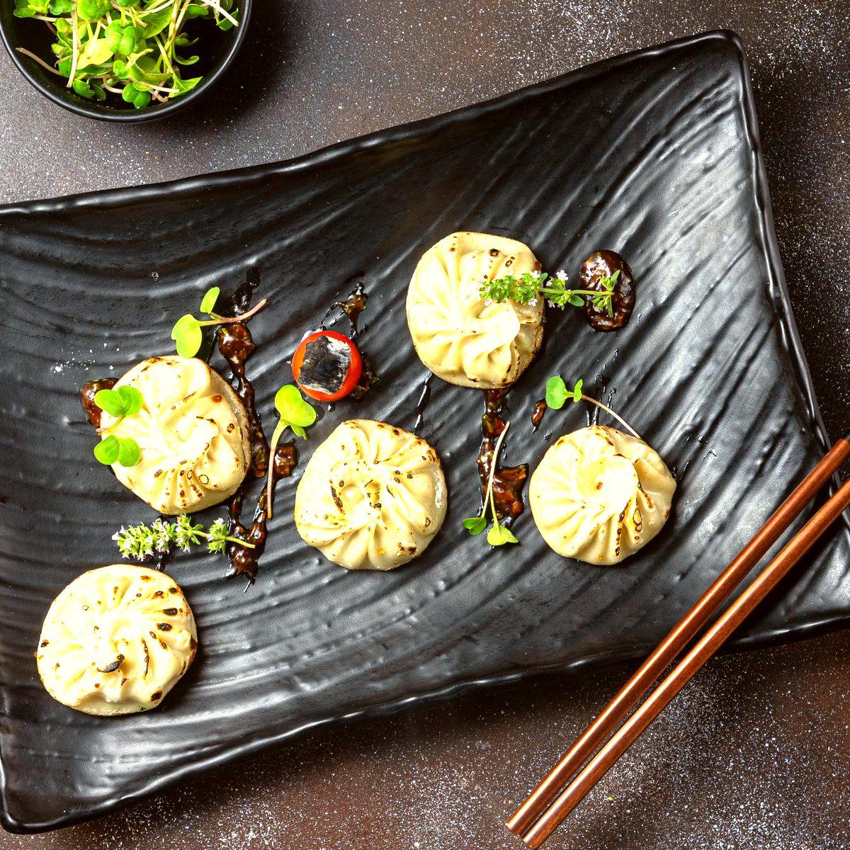 Five steamed momo dumplings on a dark plate, garnished with herbs