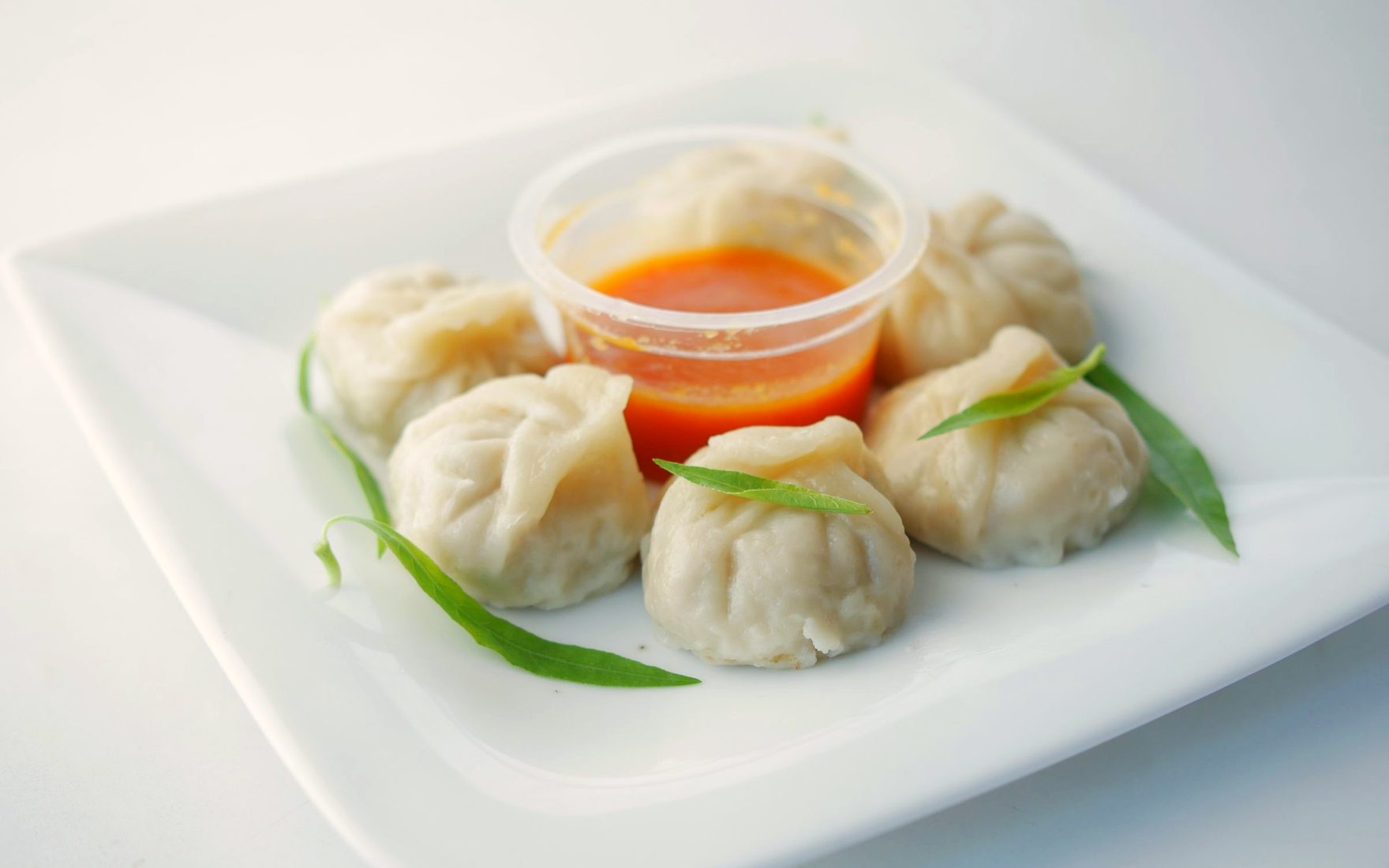 Steamed Nepalese momos with chilli dipping sauce on a white plate